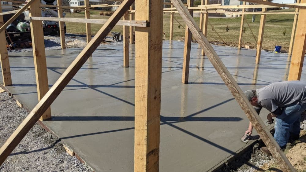 Construction worker smoothing freshly poured concrete slab under wooden framework.