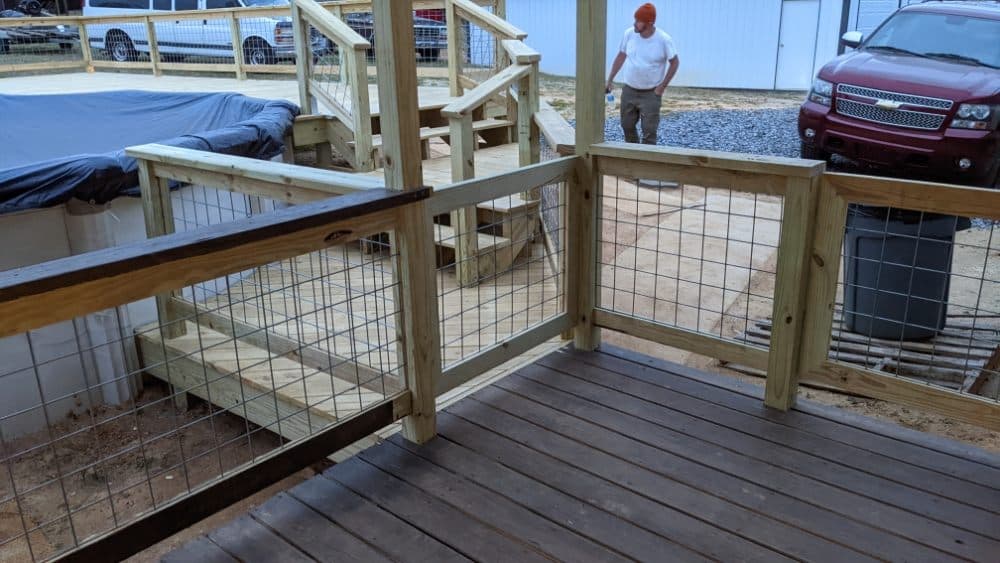 Wooden deck with a railing and a man walking nearby; pool cover visible in background.