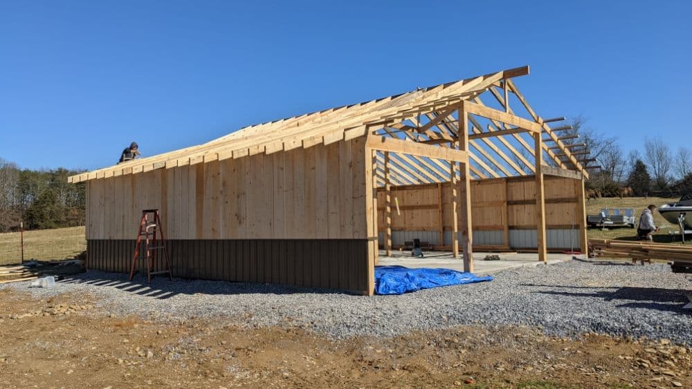 Construction of a wooden barn with a clear blue sky background and gravel ground.