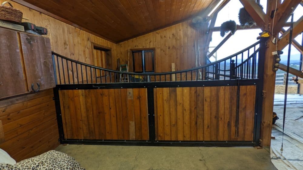Wooden horse stable interior with black metal gate and rustic decor accents.