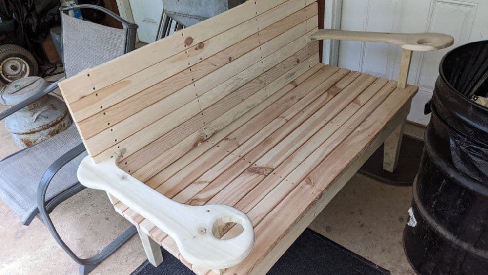 Wooden bench with curved armrests, unfinished, set in a garage environment.